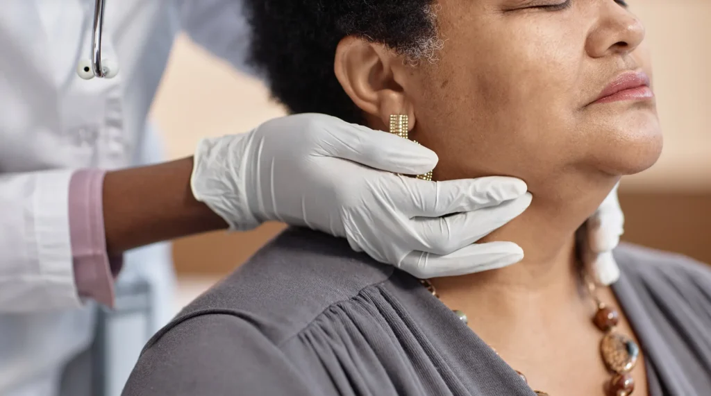 Hands of a physician palpating a patient's neck during an exam.