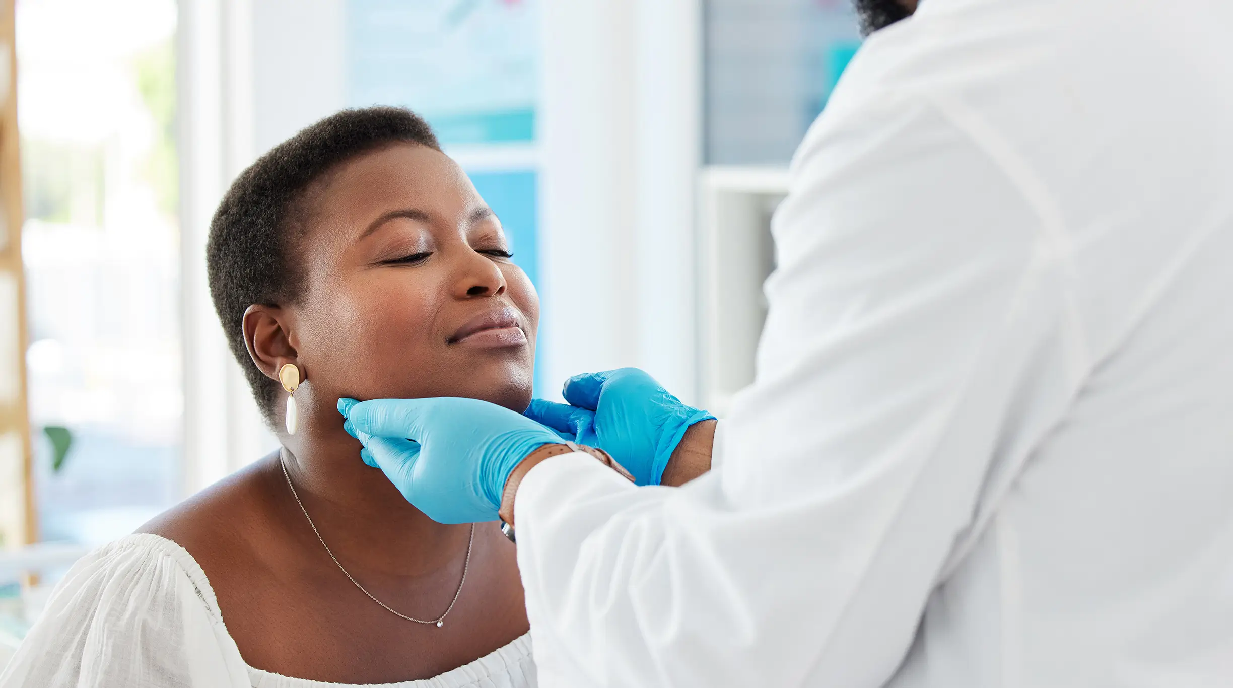 A doctor checks a woman's thyroid during a medical examination in a doctor's office.