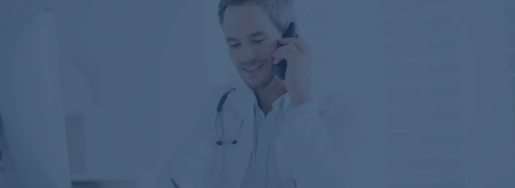 A man dressed in a white coat is conversing on a cell phone, indicating a professional setting.